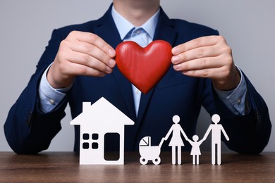 Man holding figure of heart above family at wooden table. closeup. Insurance concept