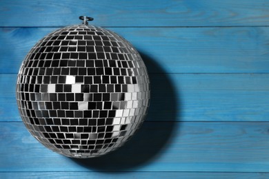 Shiny disco ball on blue wooden background, top view. Space for text