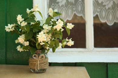 Photo of Bouquet of beautiful jasmine flowers in vase on wooden table near window outdoors, space for text