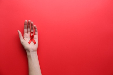 Woman holding red awareness ribbon on color background, top view with space for text. World AIDS disease day