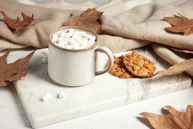 Cup of hot cozy drink, tasty cookies and  autumn leaves on table