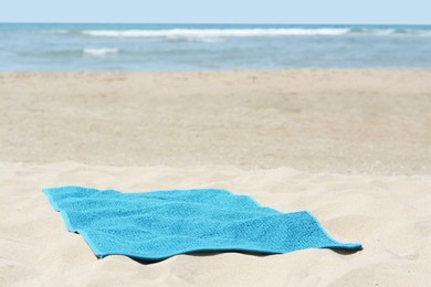 Soft blue towel on sandy beach near sea, space for text