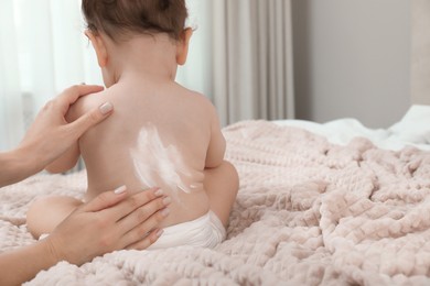 Mother applying body cream on her baby indoors, space for text