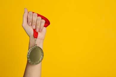 Woman holding golden medal on yellow background, closeup. Space for design