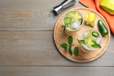 Photo of Glasses of spicy cocktail with jalapeno, carambola and mint on wooden table, flat lay. Space for text