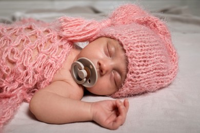 Cute newborn baby in warm hat sleeping on light bedsheet