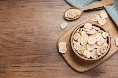 Bowl and spoon with dried banana slices on wooden table, flat lay. Space for text