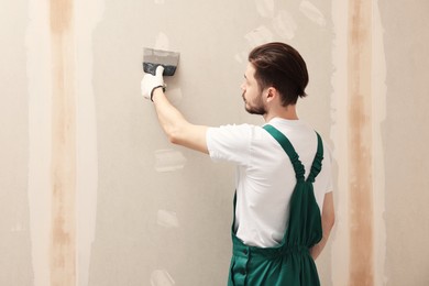 Photo of Worker in uniform plastering wall with putty knife indoors