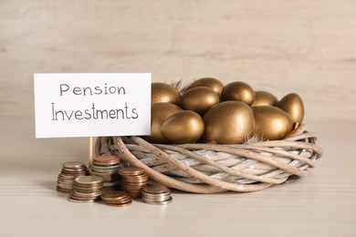 Golden eggs in nest, coins and card with phrase Pension Investments on white wooden table