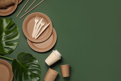Flat lay composition with disposable tableware and monstera leaves on dark green background. Space for text