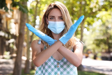 Woman in protective face mask showing stop gesture outdoors. Prevent spreading of coronavirus