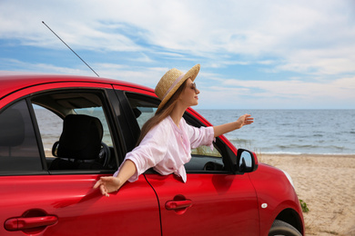 Happy woman leaning out of car window on beach. Summer vacation trip