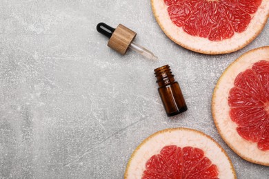 Bottle of essential oil with grapefruit slices on grey table, flat lay. Space for text