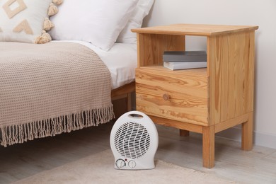 Photo of Modern electric fan heater near bedside table indoors