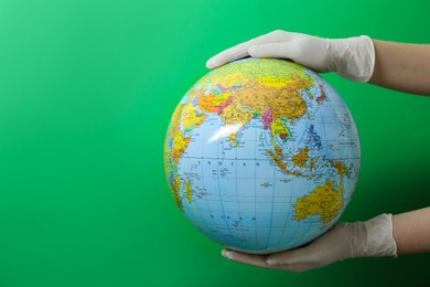Doctor in surgical gloves holding globe against green background, closeup. Space for text