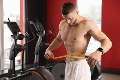 Photo of Athletic man measuring waist with tape in gym