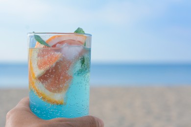Photo of Woman holding glass of refreshing drink with grapefruit and mint at beach, closeup. Space for text