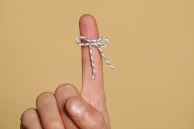 Photo of Man showing index finger with tied bow as reminder on beige background, closeup