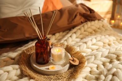 Photo of Air reed freshener and burning candles on bed indoors. Interior elements