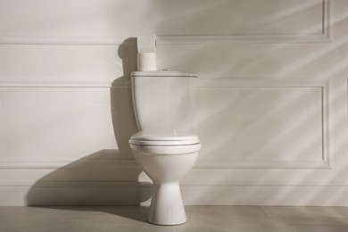 Modern toilet bowl and paper rolls near white wall in restroom. Interior design