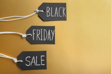Tags with words BLACK FRIDAY SALE on golden background, flat lay. Space for text