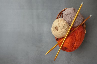 Different balls of woolen knitting yarns and needles on grey background, top view. Space for text