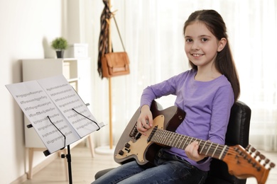 Little girl playing guitar at music lesson. Learning notes