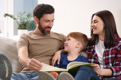 Happy parents with their child reading book on couch at home