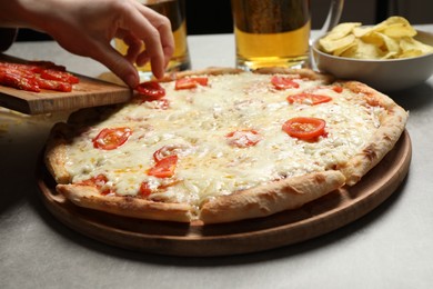 Photo of Woman putting tomato onto pizza Margherita at table, closeup