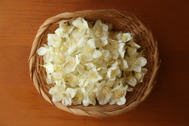 Beautiful white jasmine flowers in wicker basket on wooden table, top view