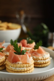 Delicious crackers with cream cheese, prosciutto and parsley on plate, closeup