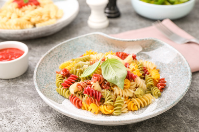 Colorful pasta with basil and cheese on grey table, closeup
