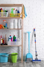 Shelving unit with detergents, cleaning tools and toilet paper near white brick wall indoors