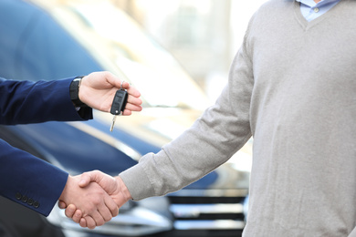 Salesman giving key to customer while shaking hands in modern auto dealership, closeup. Buying new car