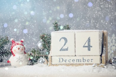 Photo of December 24 - Christmas Eve. Snow falling onto wooden block calendar and festive decor against blurred lights