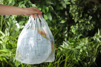 Woman holding globe in plastic bag against green leaves, closeup. Space for text. Environmental conservation
