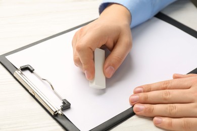 Man erasing something on paper at white wooden table, closeup