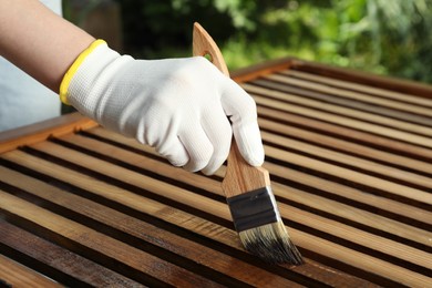 Woman applying wood stain onto planks outdoors, closeup