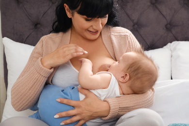 Photo of Woman breastfeeding her little baby on bed indoors