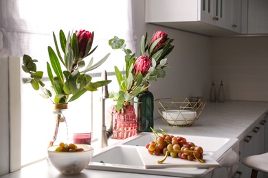 Photo of Vases with beautiful protea flowers near sink in kitchen. Interior design