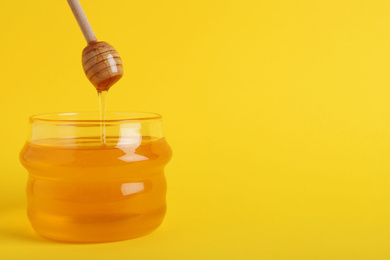 Jar with organic honey and dipper on yellow background. Space for text