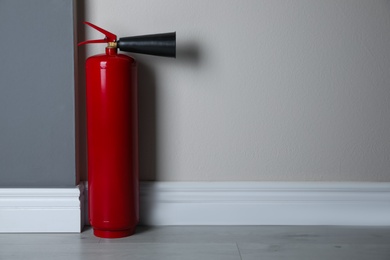 Fire extinguisher near light wall indoors. Space for text