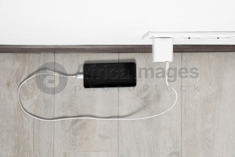 Modern smartphone charging from electric socket indoors, top view