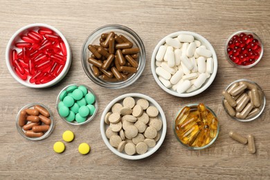 Photo of Different dietary supplements in bowls on wooden table, flat lay