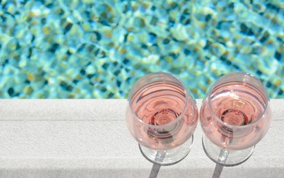 Photo of Glasses of tasty rose wine on swimming pool edge, above view. Space for text