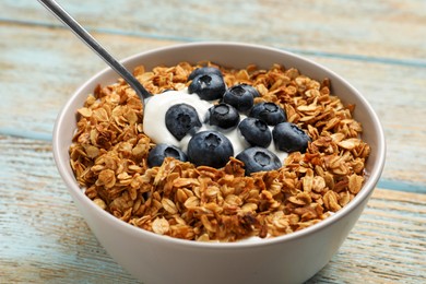 Bowl of yogurt with granola and blueberries on old wooden table, closeup