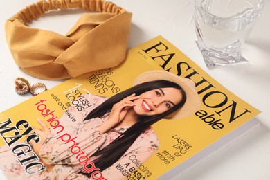 Fashion magazine, accessories and glass of water on white table