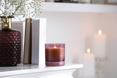 Photo of Burning candle, flowers and books on white table indoors