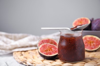 Glass jar of tasty sweet fig jam with spoon and fruits on table. Space for text