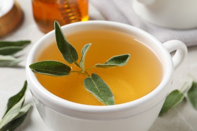 Cup of aromatic sage tea with fresh leaves on table, closeup